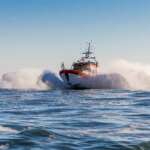 A Swedish Sea Rescue Society rescue boat travelling at speed across open water during an operational response, with waves and sea spray surrounding the vessel